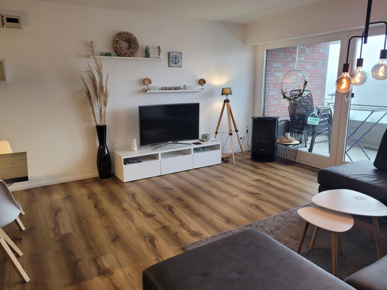 Wohnzimmer mit Fernseher, Holzboden und Balkonzugang.