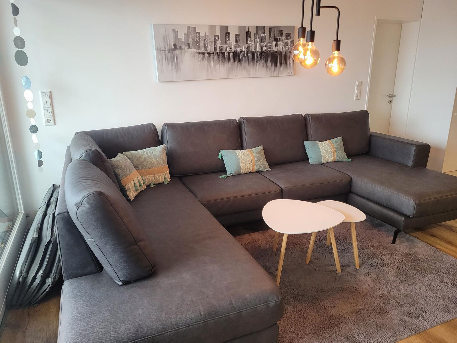Ein großes L-Förmiges Sofa mit Kissen, zwei runde Tische und eine Wanddekoration.