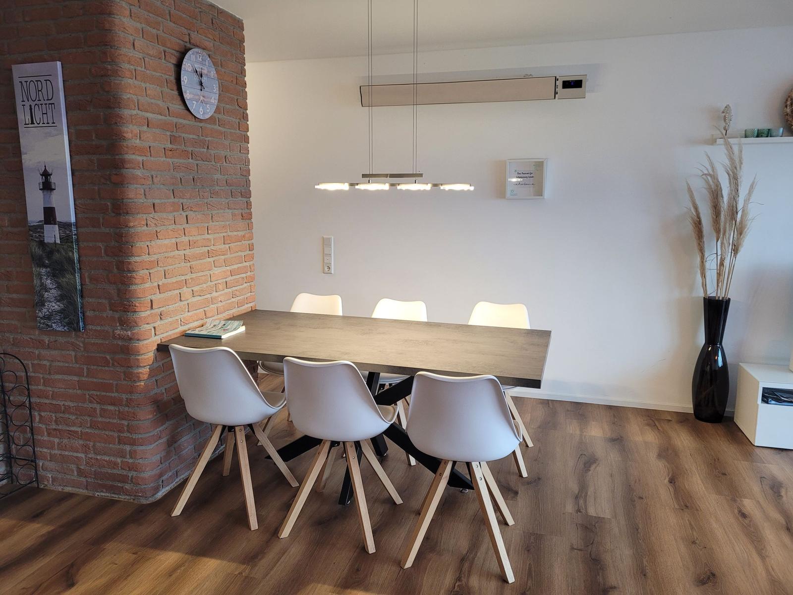 Esstisch mit sechs Stühlen, Holzboden und Backsteinwand mit Uhr und Bild.
