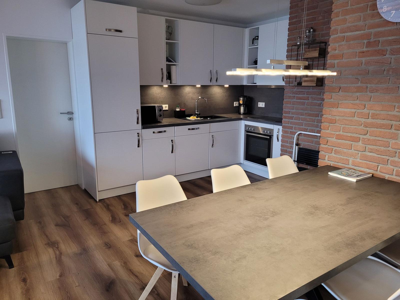 Küche mit Essbereich, weiße Schränke, Backofen und Backsteinwand.
