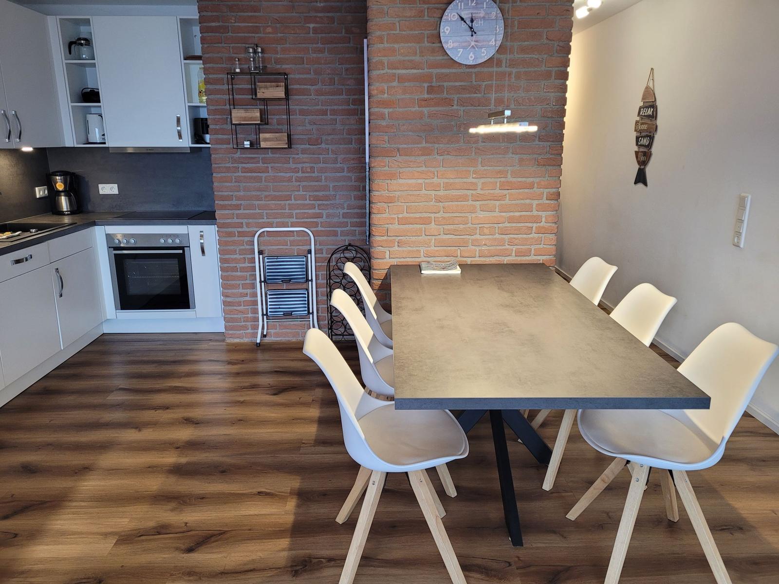 Essbereich mit Tisch und Stühlen, Küchenzeile und Backofen im Hintergrund.