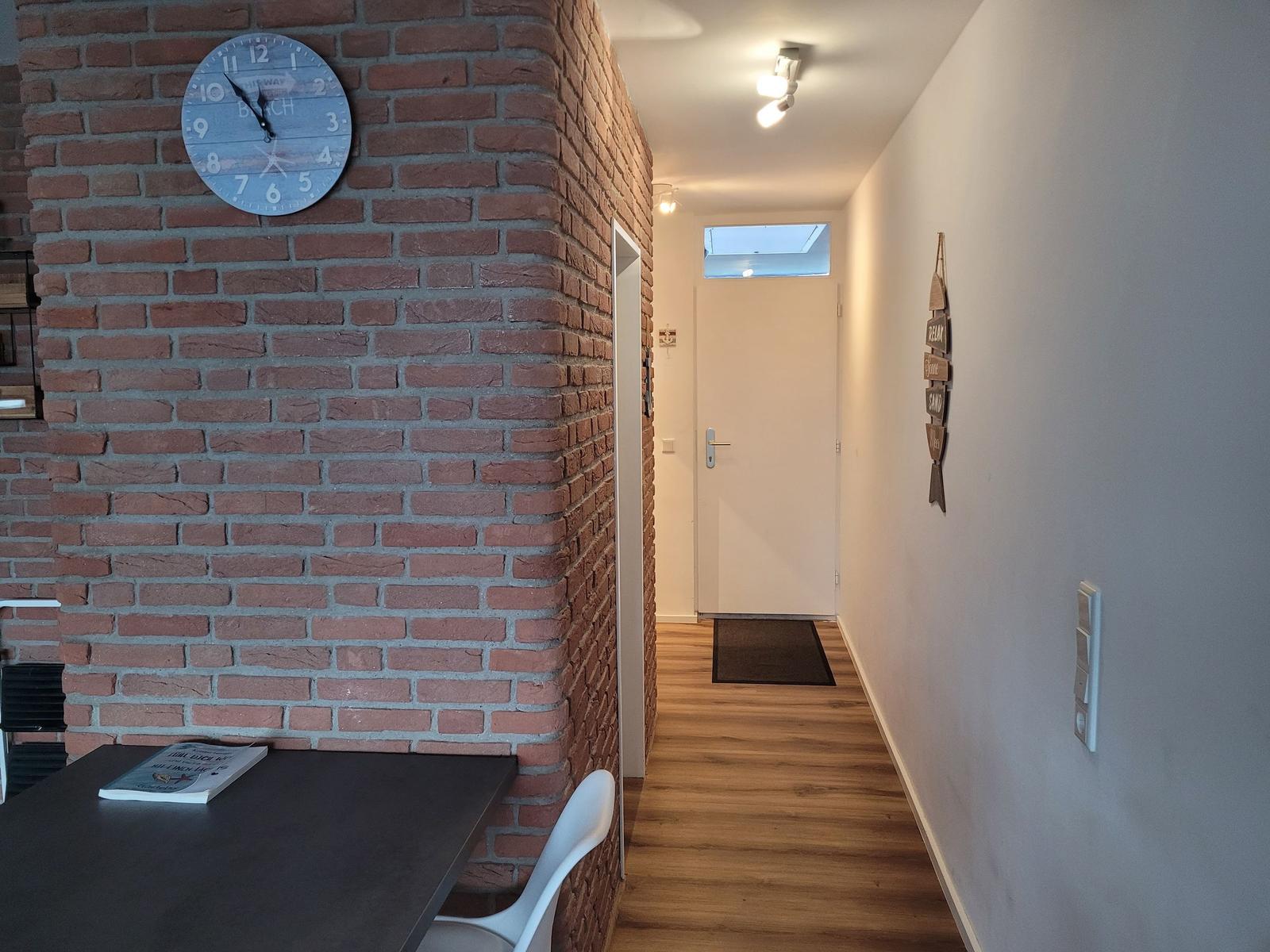 Hallenflur mit Holzboden, Backsteinwand und Wanduhr. Tür zum Eingangsbereich.