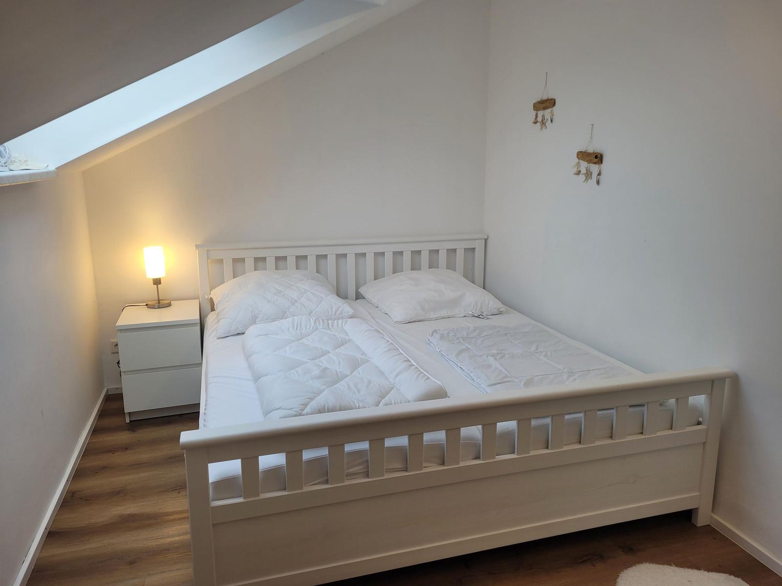 Schlafzimmer mit weißem Bett, Nachttisch und Lampe unter Dachschräge.