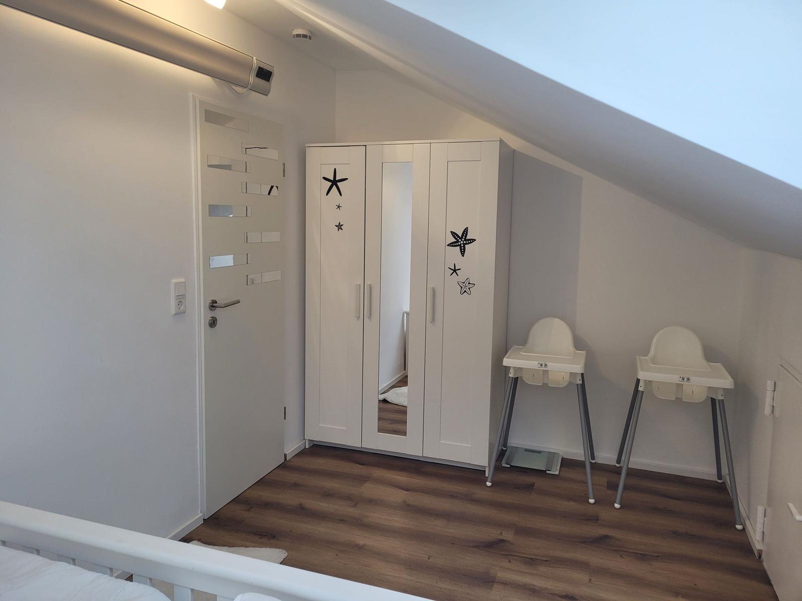 Schlafzimmer mit Kleiderschrank, Hochstuhl und Holzboden unter Dachschrägen.