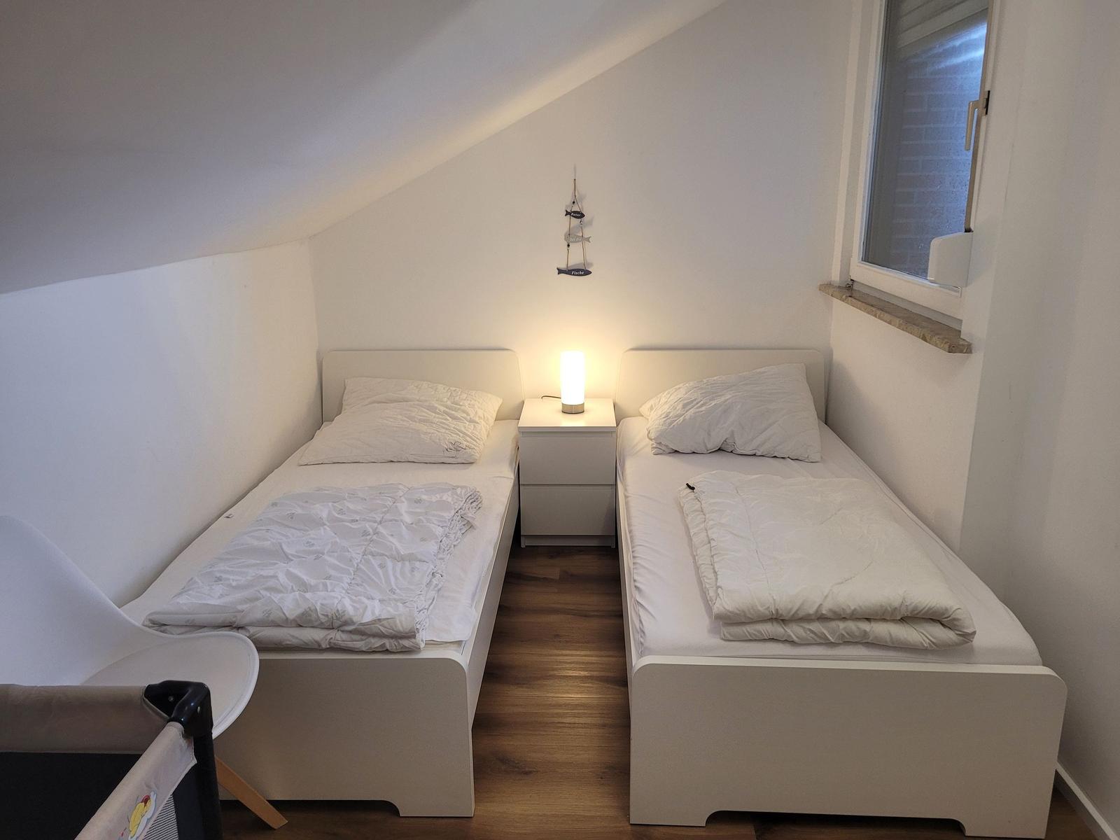 Zwei Einzelbetten mit Nachttisch und Lampe unter Dachschrägen.