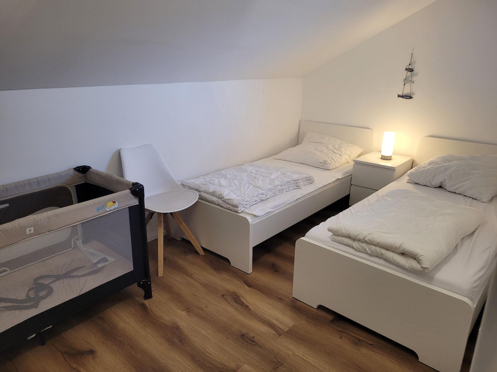 Zwei Einzelbetten, ein Kinderbett und eine Stehlampe in einem Schlafzimmer mit Holzboden.
