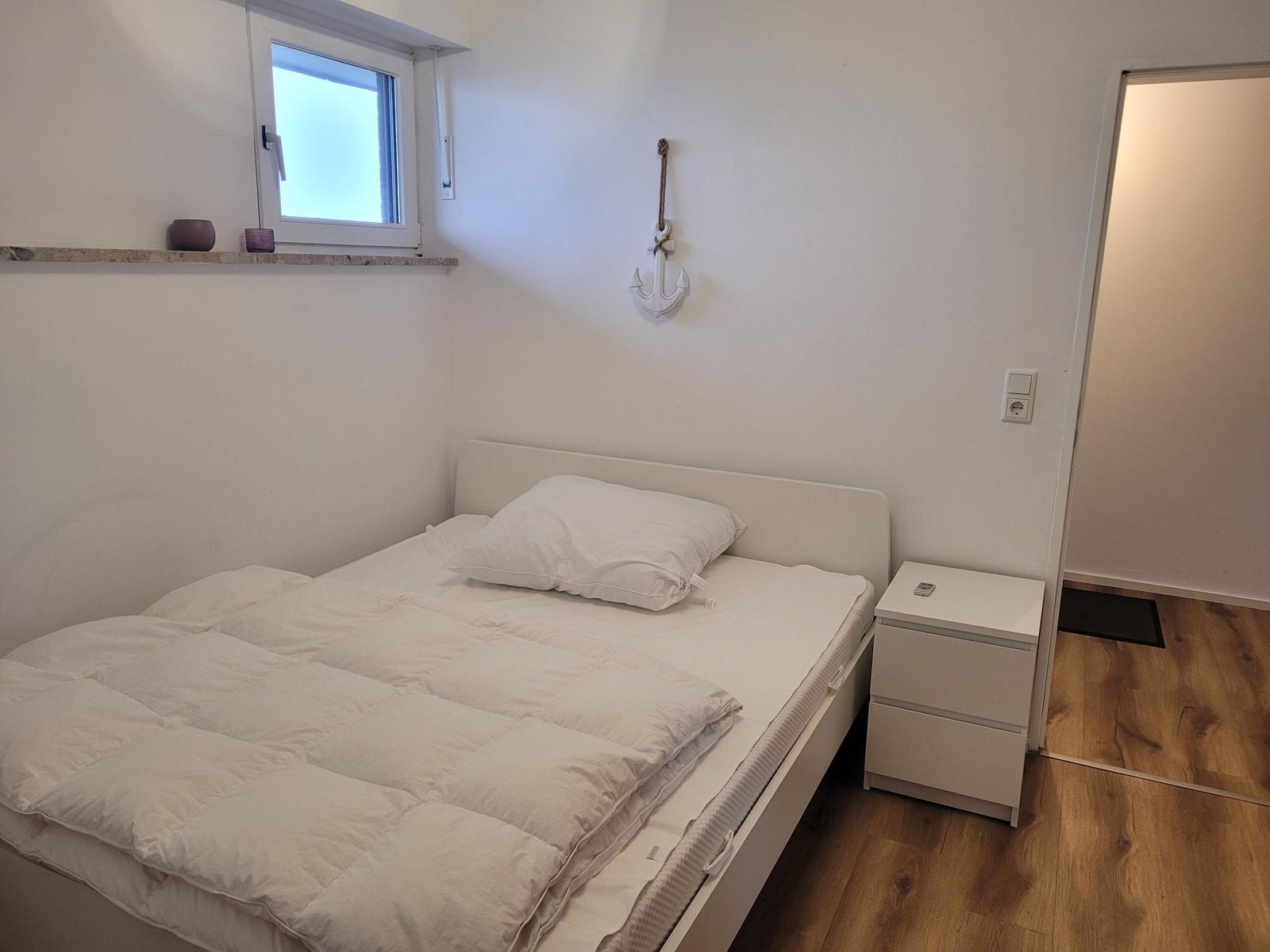 Schlafzimmer mit Bett, Nachttisch und Fenster. An der Wand hängt ein Anker.