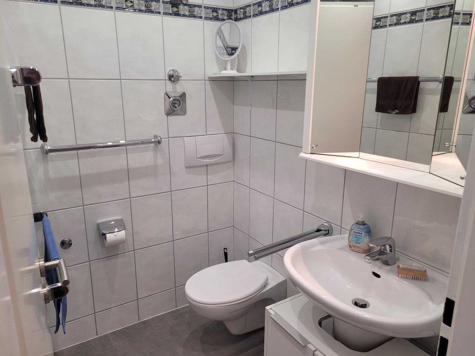 Badezimmer mit Toilette, Waschbecken und Dusche. Weiße Fliesen und Spiegelschrank.