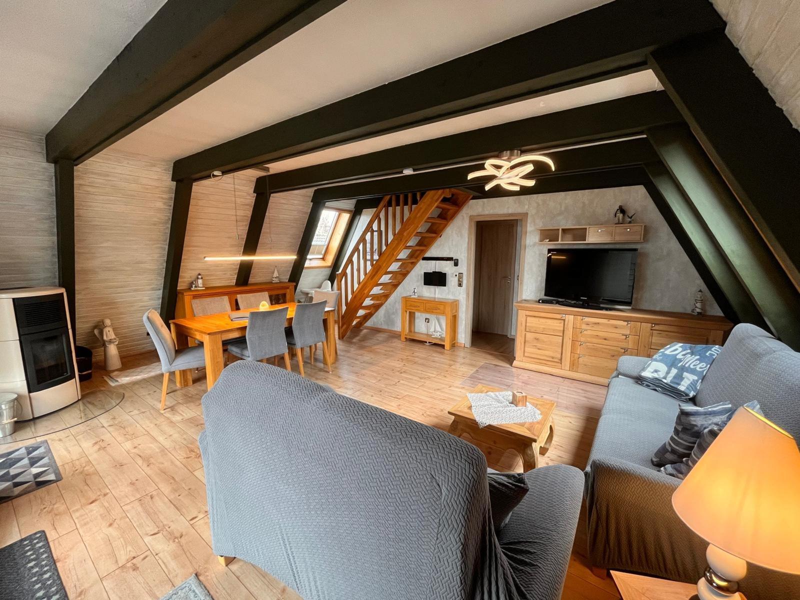 Wohn- und Essbereich mit Holzdielen, Sofa, Tisch und Stühlen sowie Treppenhaus.