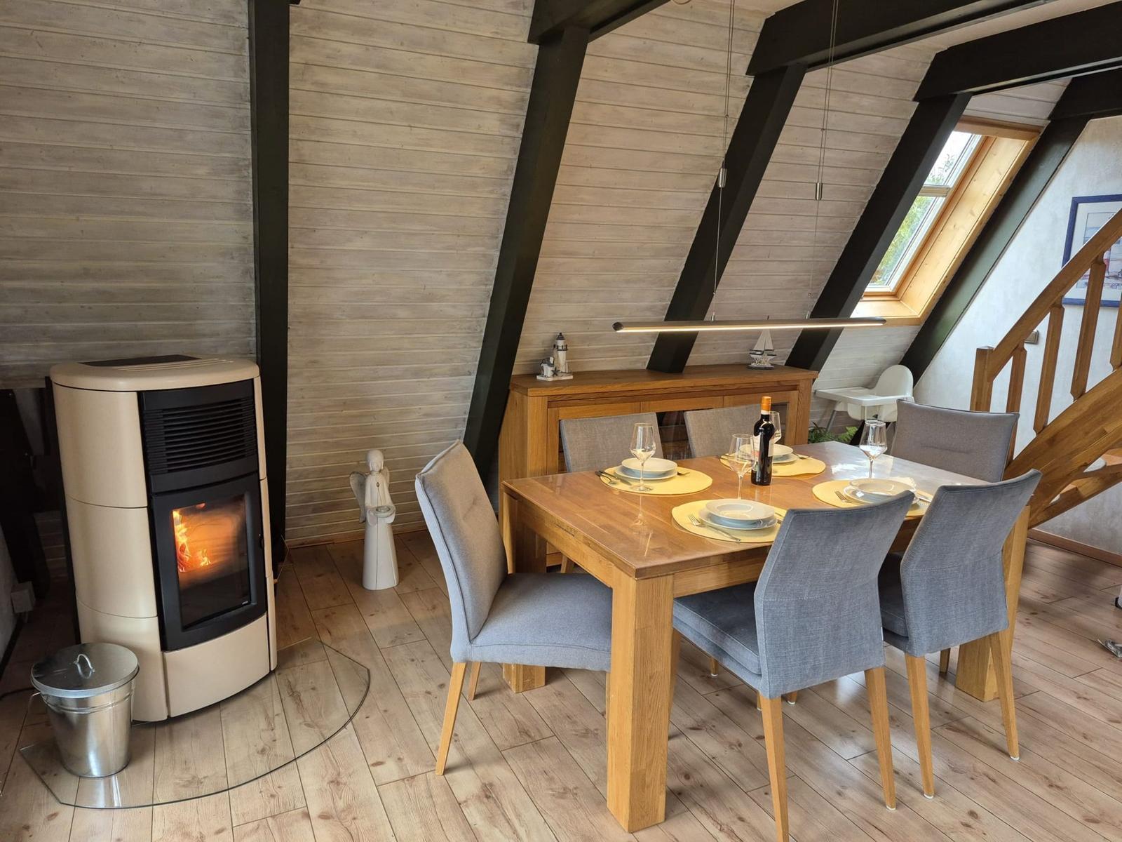 Esszimmer mit Esstisch, Stühlen und Kaminofen unter Holzdecke.