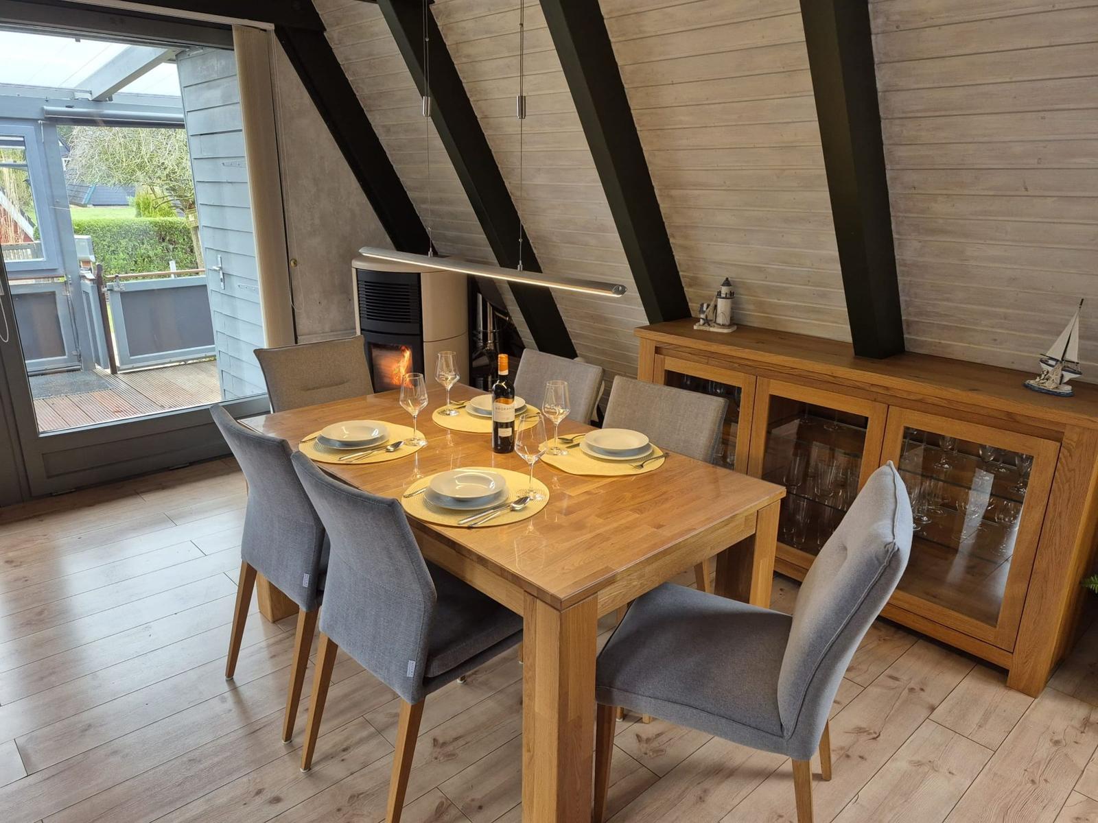 Esszimmer mit Holztisch, grauen Stühlen und Kamin. Durchgang zur Terrasse.