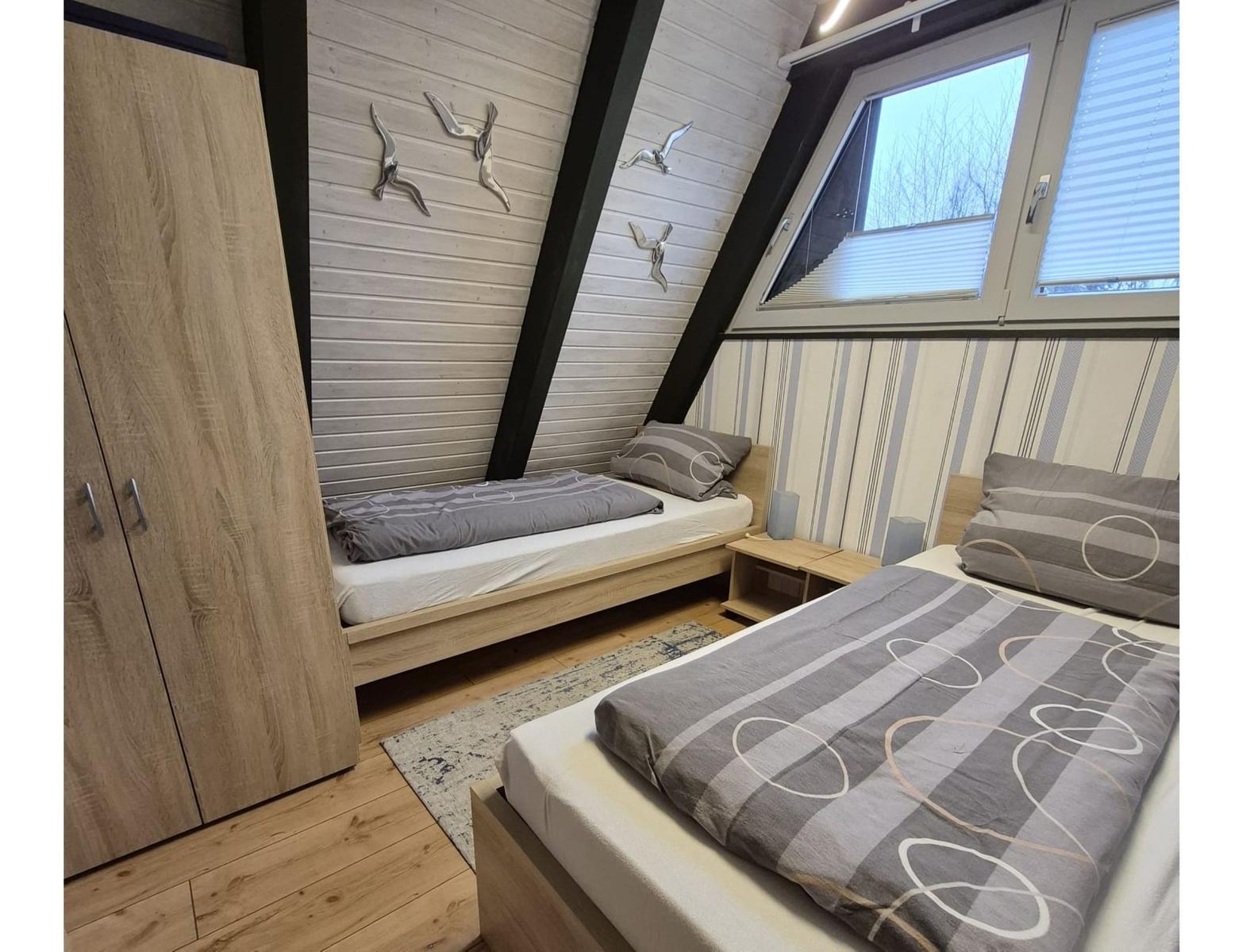 Zwei Betten mit grauer Bettwäsche, Holzmöbel und schräger Dachschräge mit Fenster.