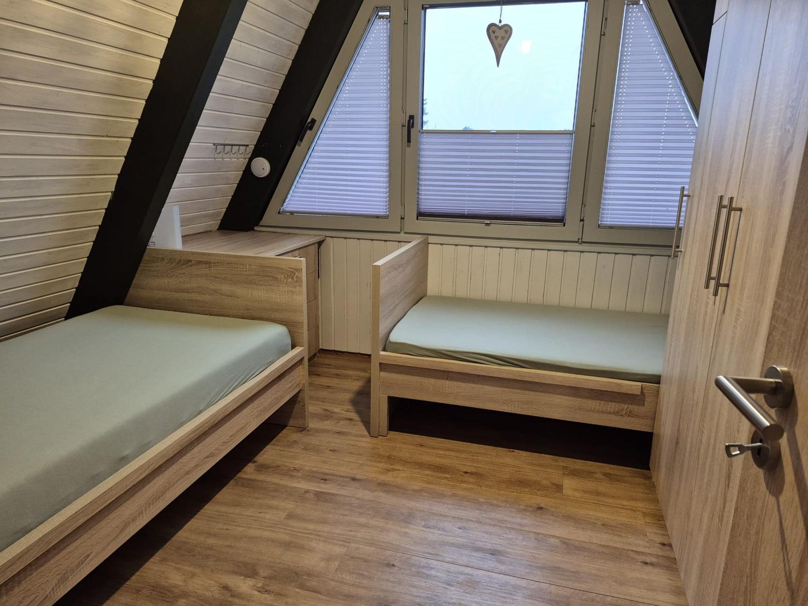 Zwei Schlafplätze in einem Dachzimmer mit Holzboden und Dachfenster.
