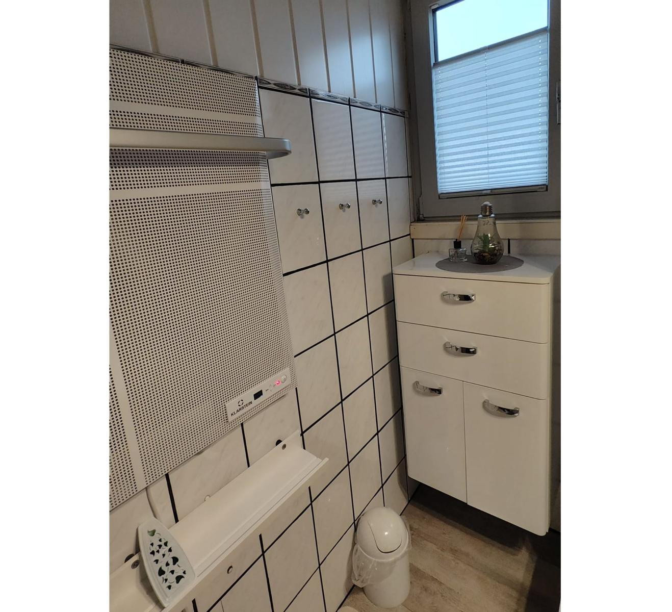 Badezimmer mit weißen Fliesen, Schrank und Fenster mit Jalousie.