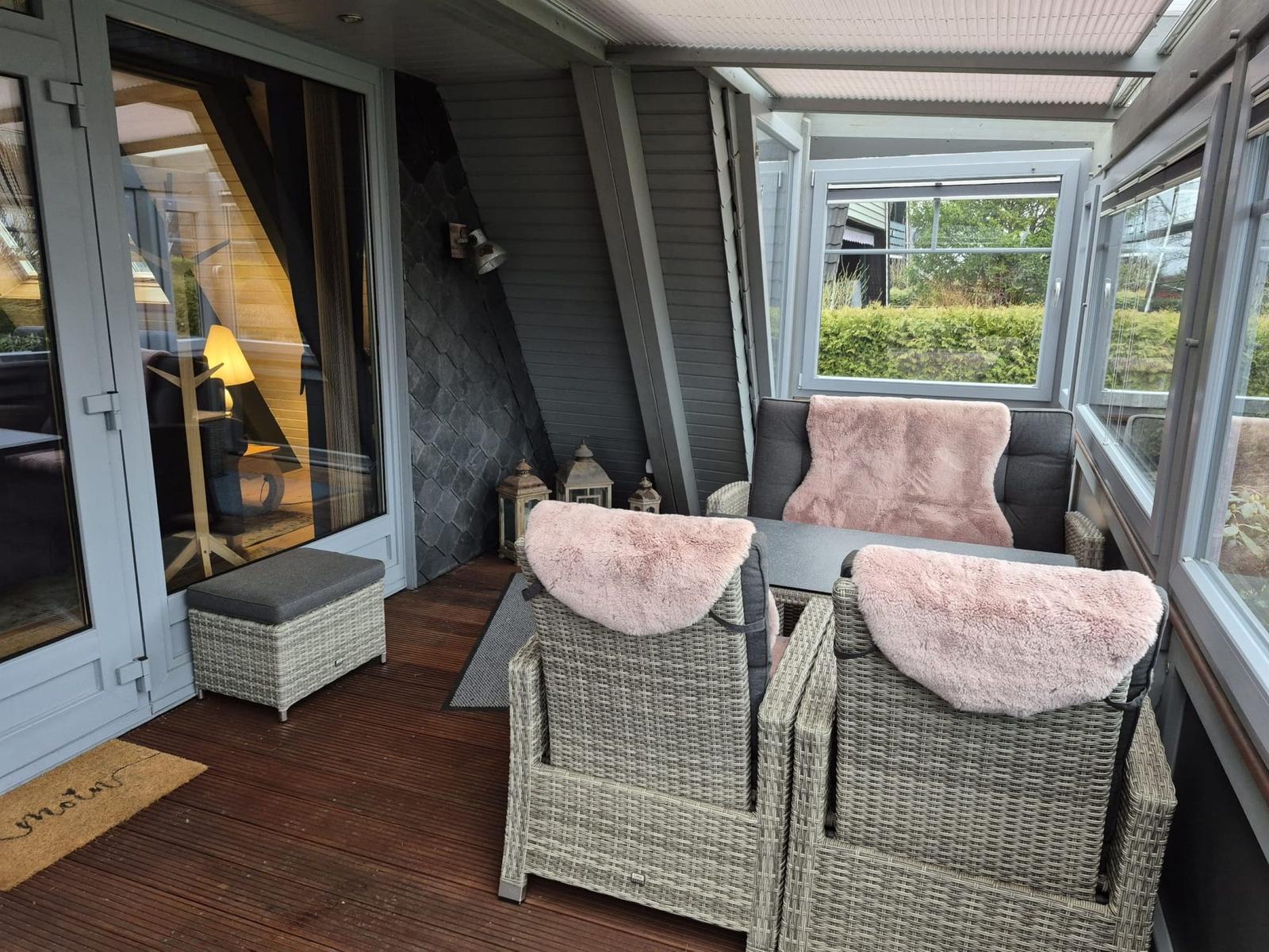 Terrasse mit Rattanmöbeln, rosa Felldecken und Holzboden. Durchgang ins Innere.