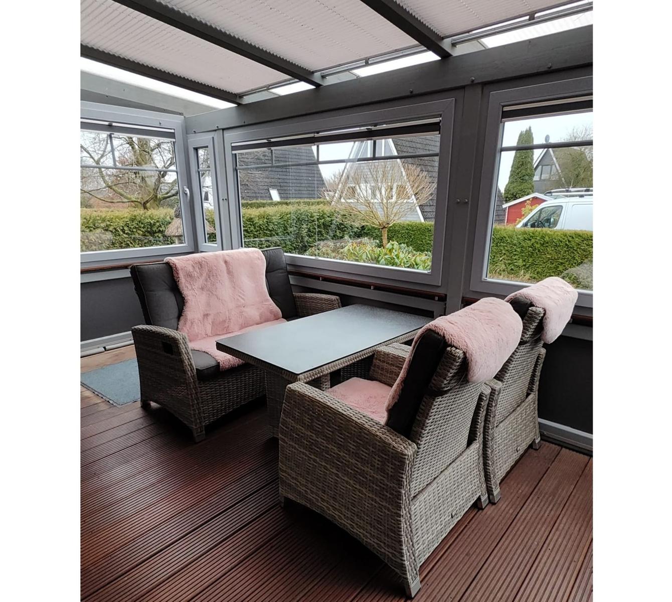 Terrasse mit Sitzgruppe, Tisch und Fenstern. Holzdecke und Außenausstattung.