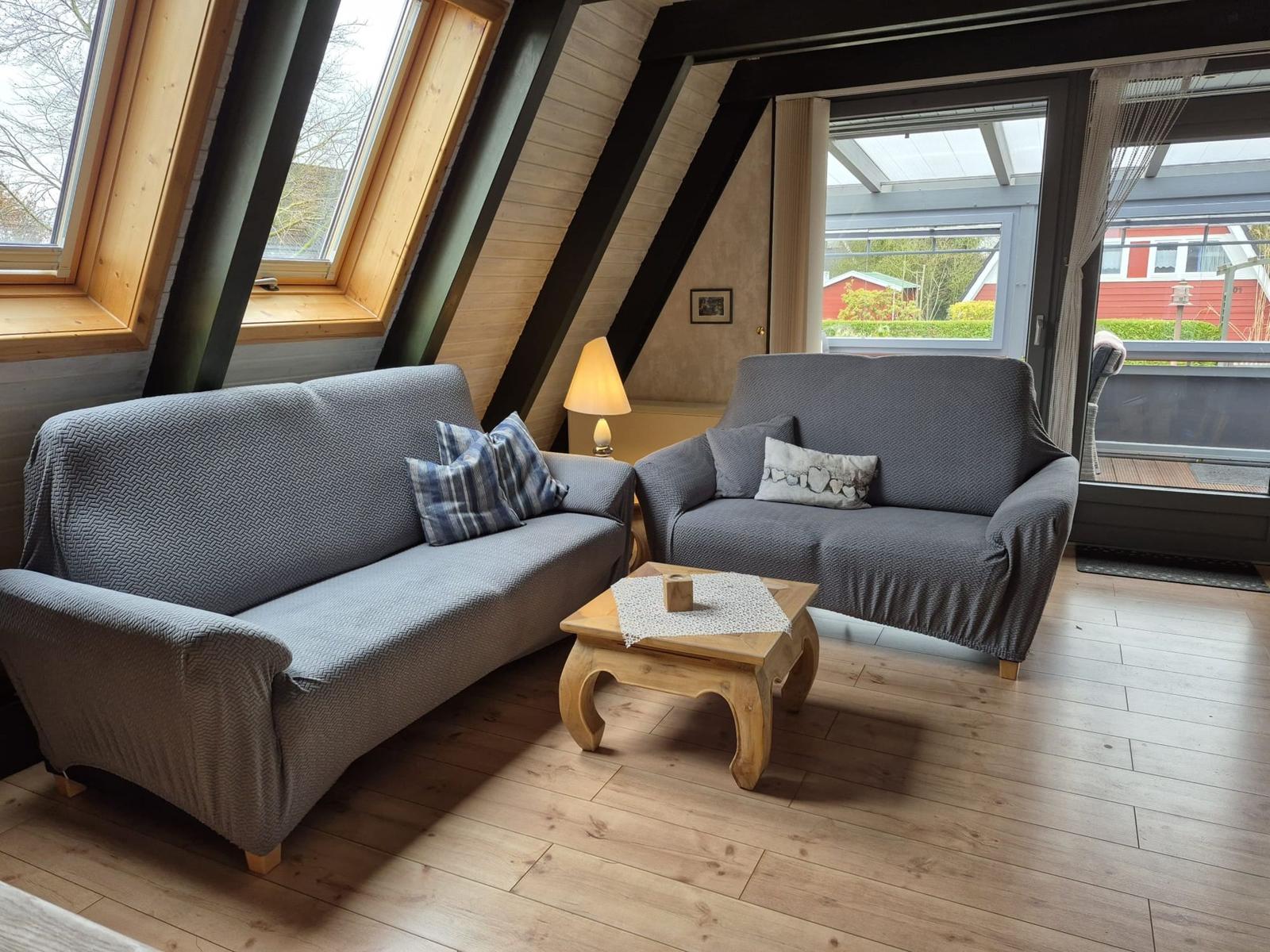 Zwei graue Sofas mit Kissen stehen vor großen Fenstern und einer Tür.