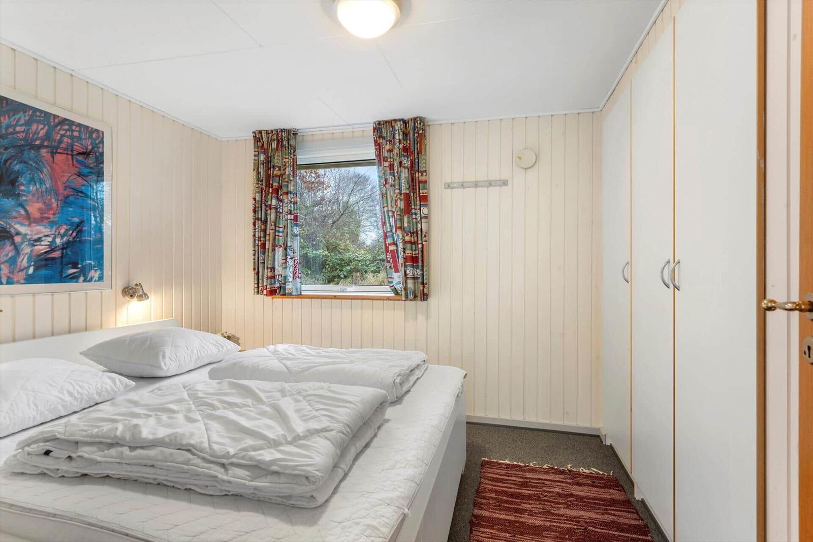 Bedroom with bed, window, and curtains. Wall art and coat rack are visible.
