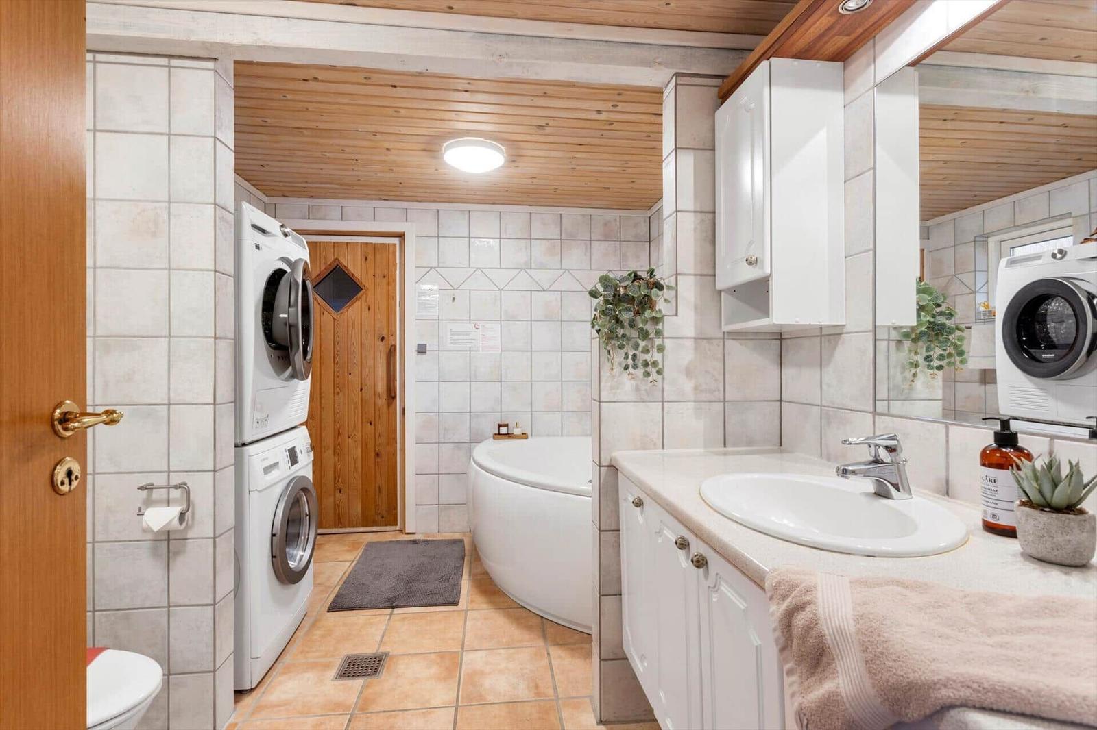 Bathroom with washing machine, bathtub, and mirror. Wooden ceiling and tiled floor.