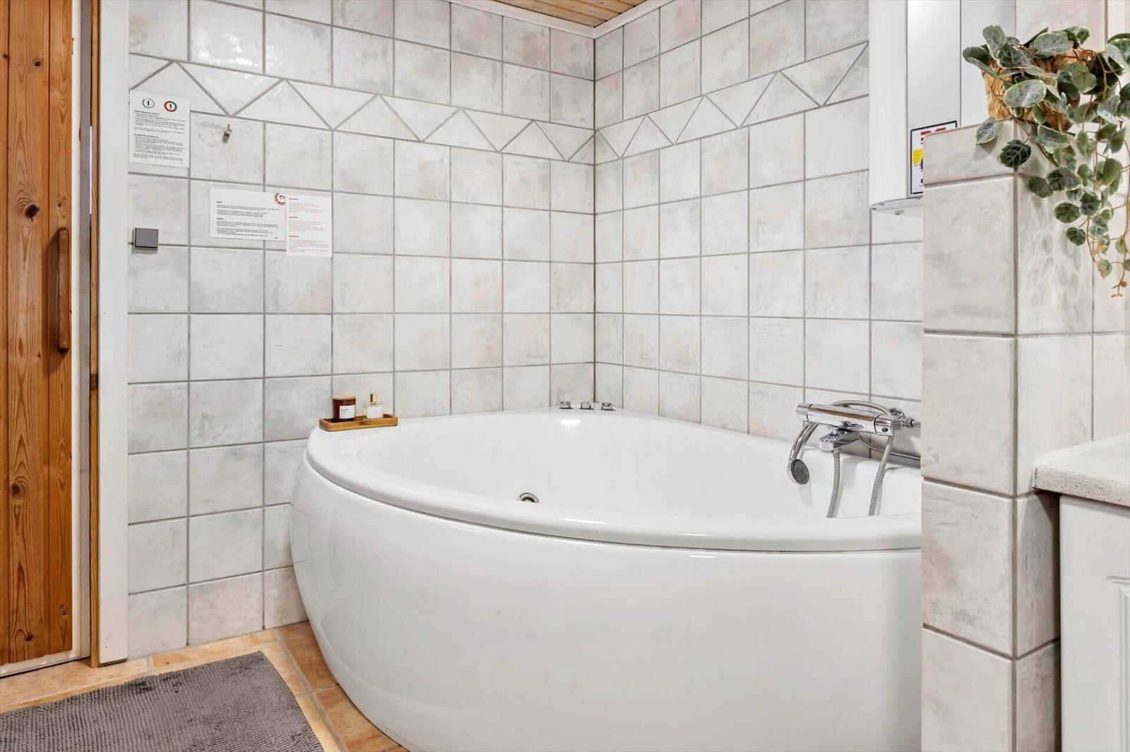 Bath with corner bathtub, tiled walls, and plant on the countertop.