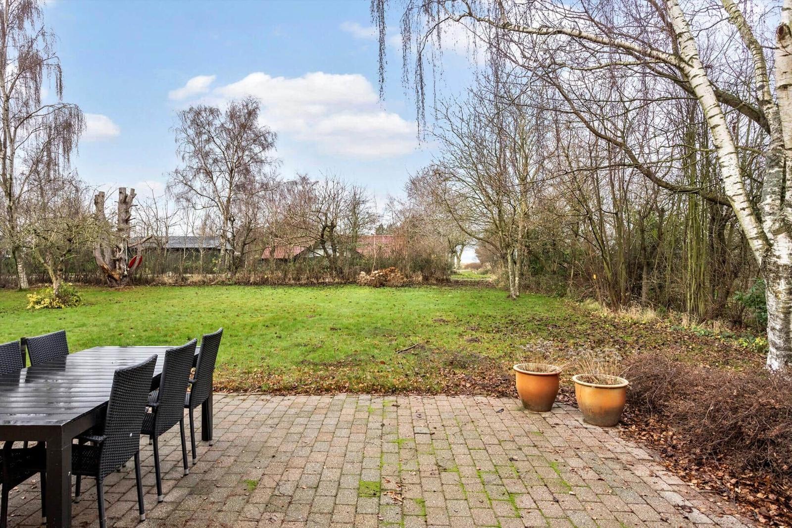 Patio with table and chairs, view of green lawn and trees.
