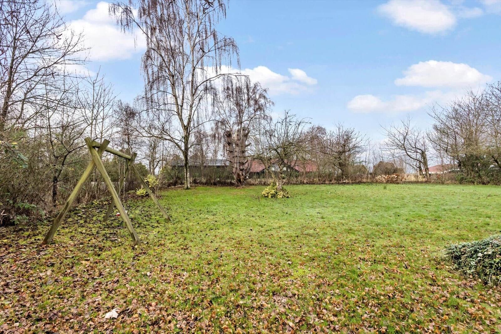 Green garden with swing set and trees under blue sky.