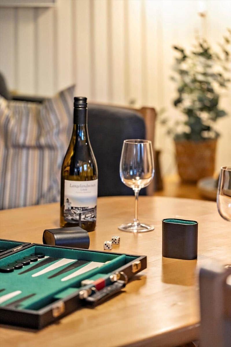 A table with backgammon, wine, and glasses. In the background, a sofa and a plant.