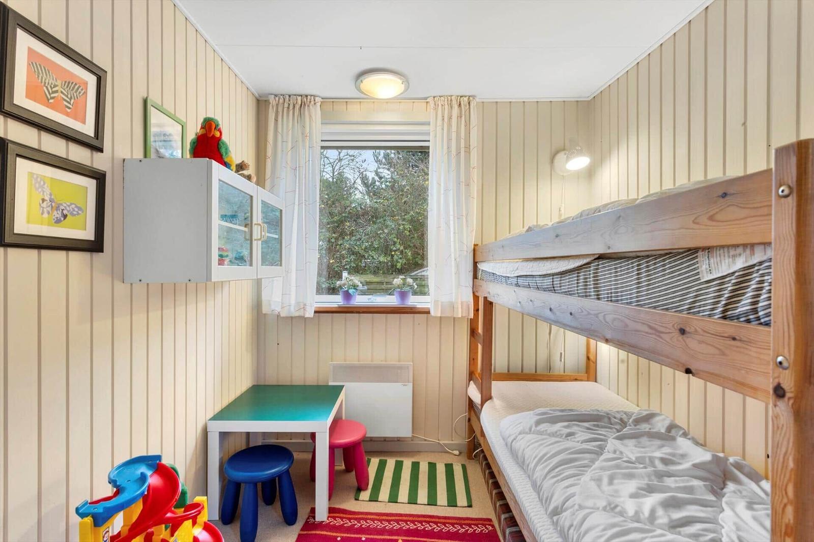 A bedroom with bunk beds, toys, and a window overlooking greenery.