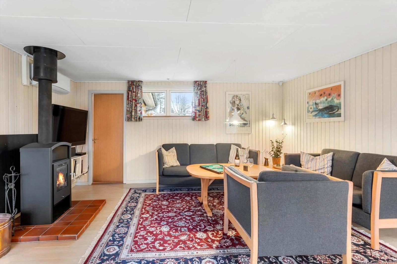 Living room with fireplace, sofa, table, and rug. Windows with curtains and wall art.