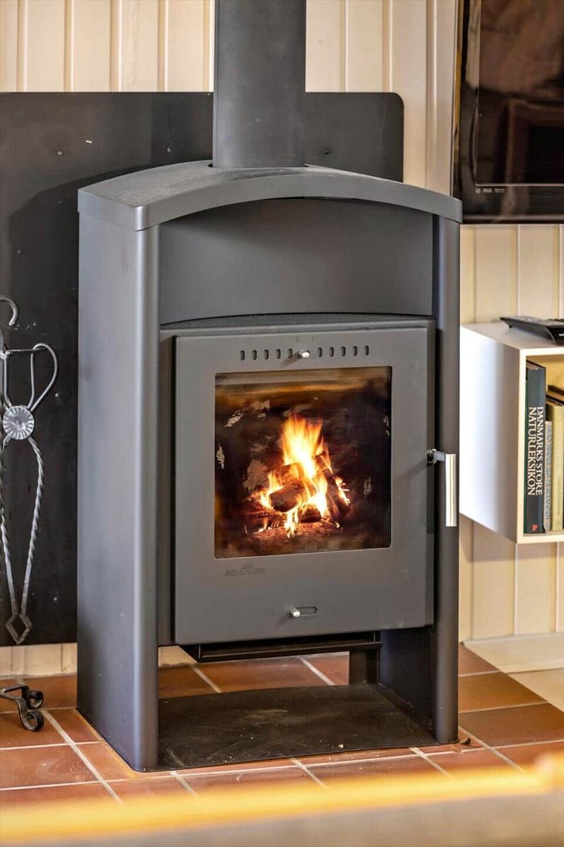 A wood-burning stove stands on tiled floor. To the left, a fireplace tool hangs.