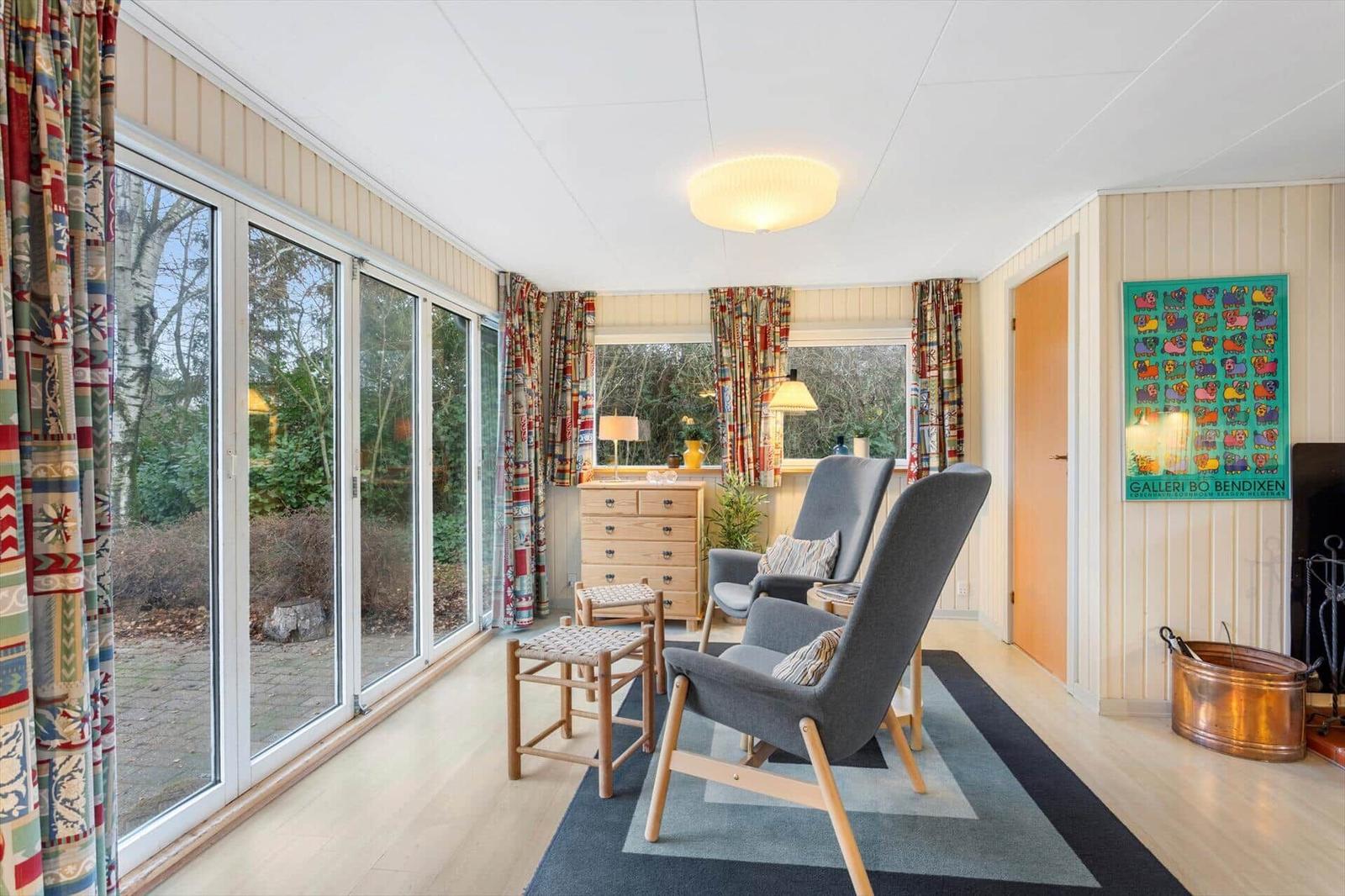 A living room with two gray chairs, a wooden dresser, and large windows.