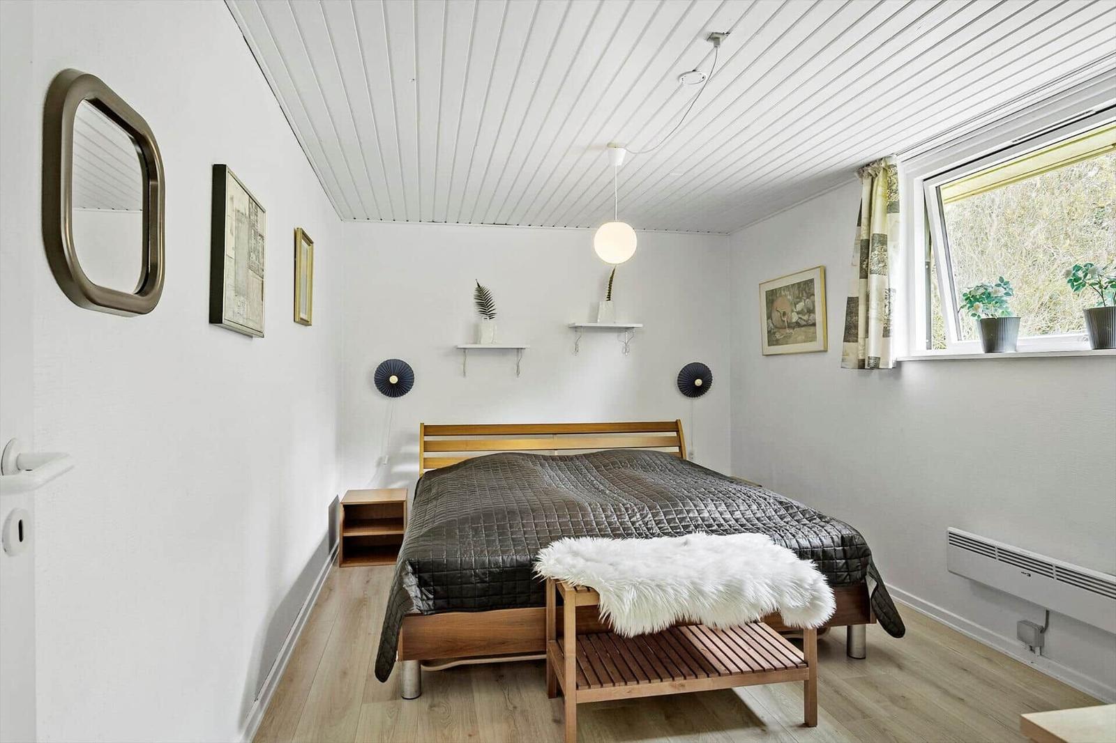 Bedroom with bed, window, wall mirrors, and wooden floor.