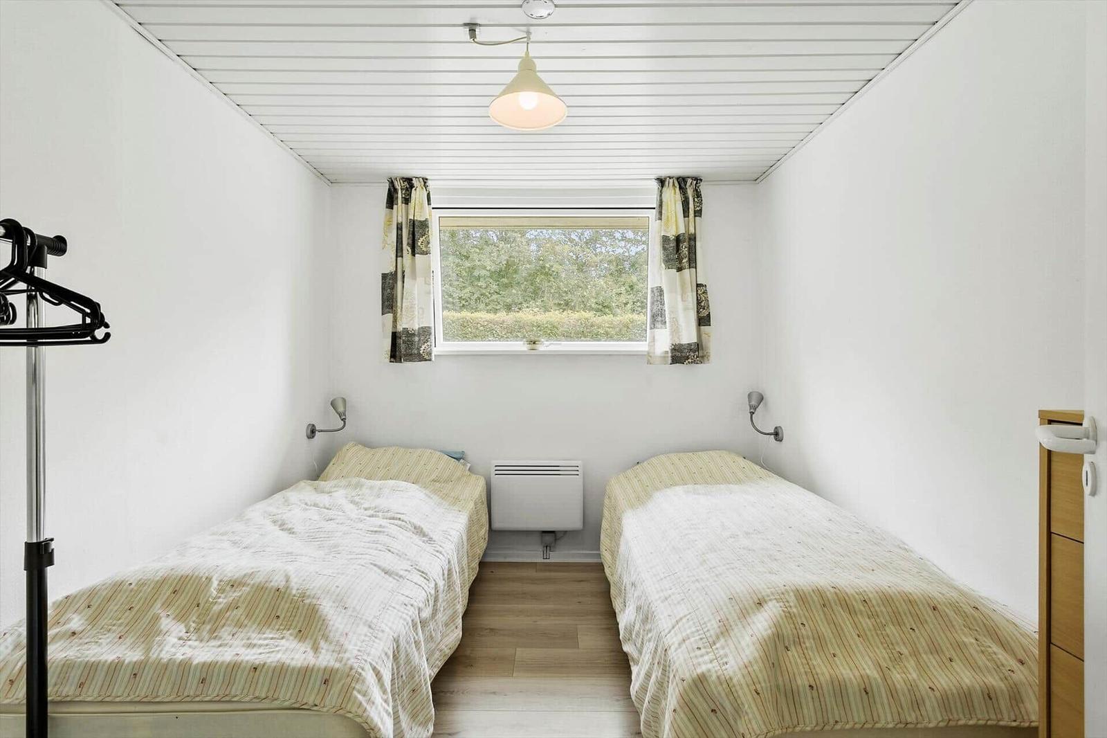 Two single beds, window with curtains, ceiling light, and clothes rack.