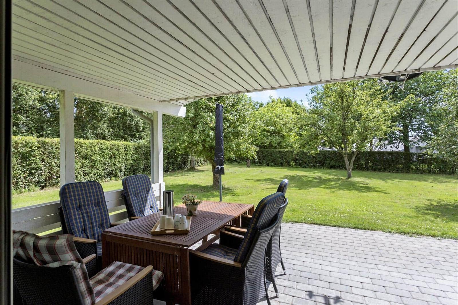 Patio with table and chairs, view of green lawn and trees.