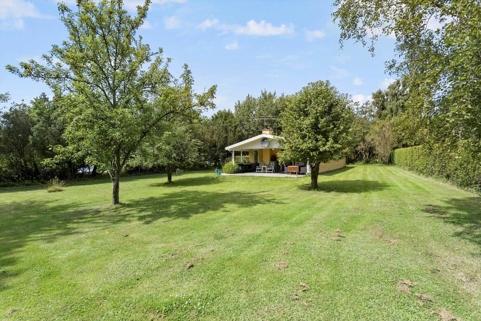 A yellow house with a terrace stands on a green lawn between trees.