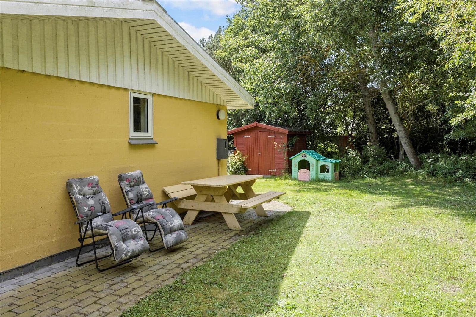 Yellow house with seating and picnic table in garden. Backyard with playhouse and shed.