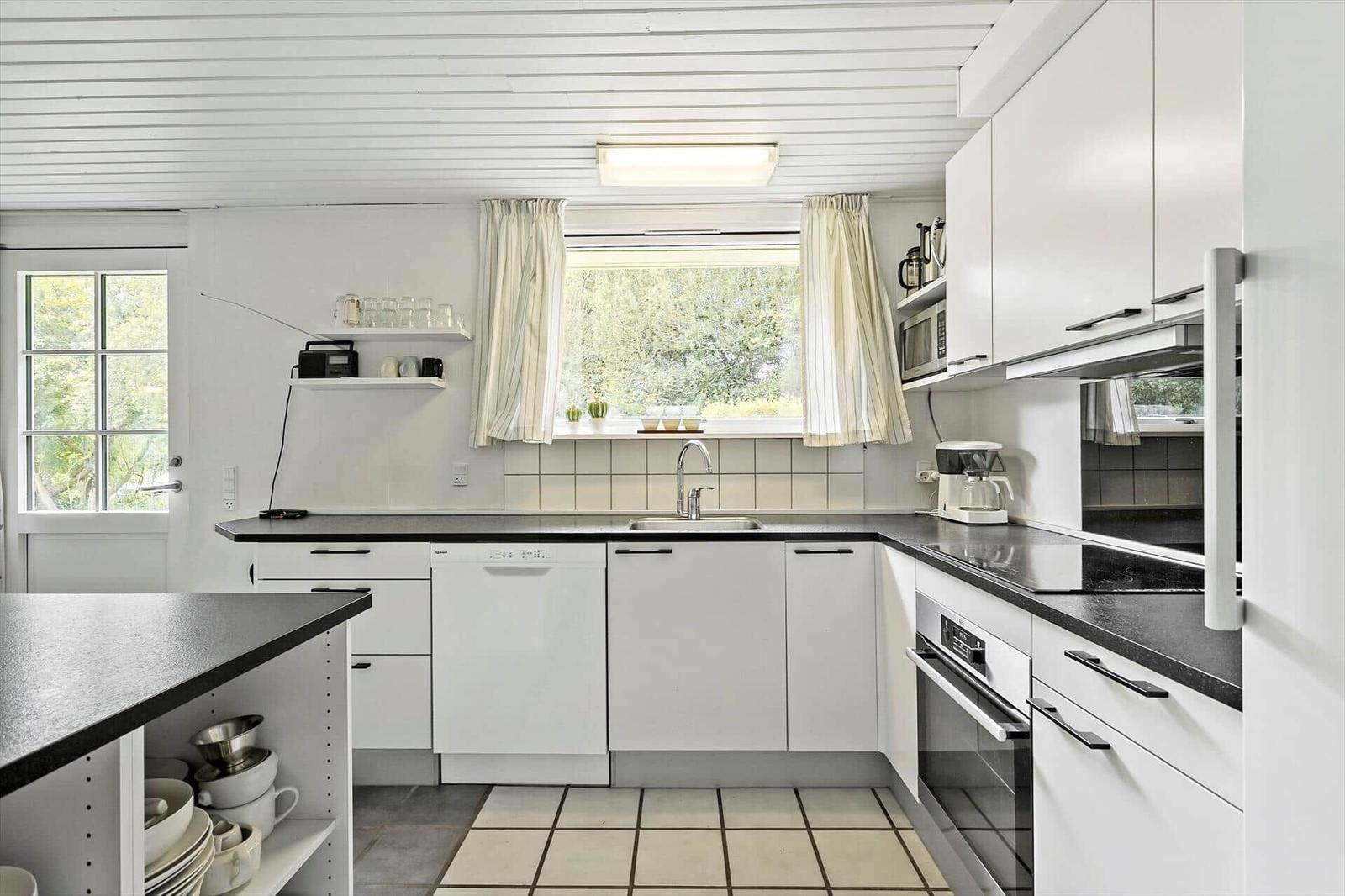 Kitchen with white cabinets, black countertops, and window with view of greenery.