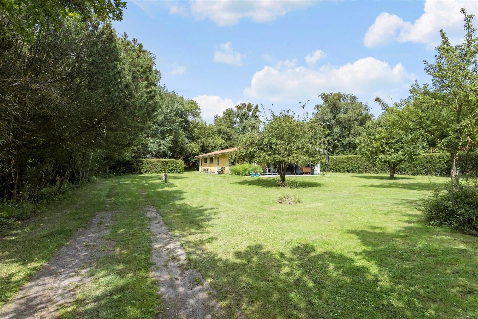 House with garden, terrace, and trees under blue sky.