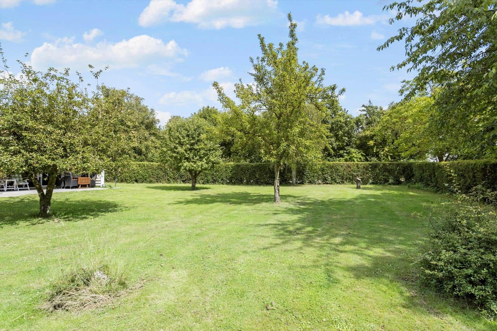 Large green garden with trees and hedge. Outdoor table and chairs are visible.