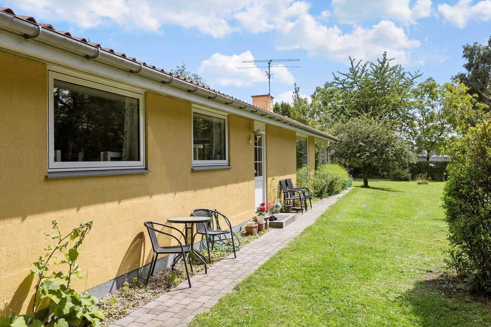 Yellow house with patio, garden, and seating area under blue sky.
