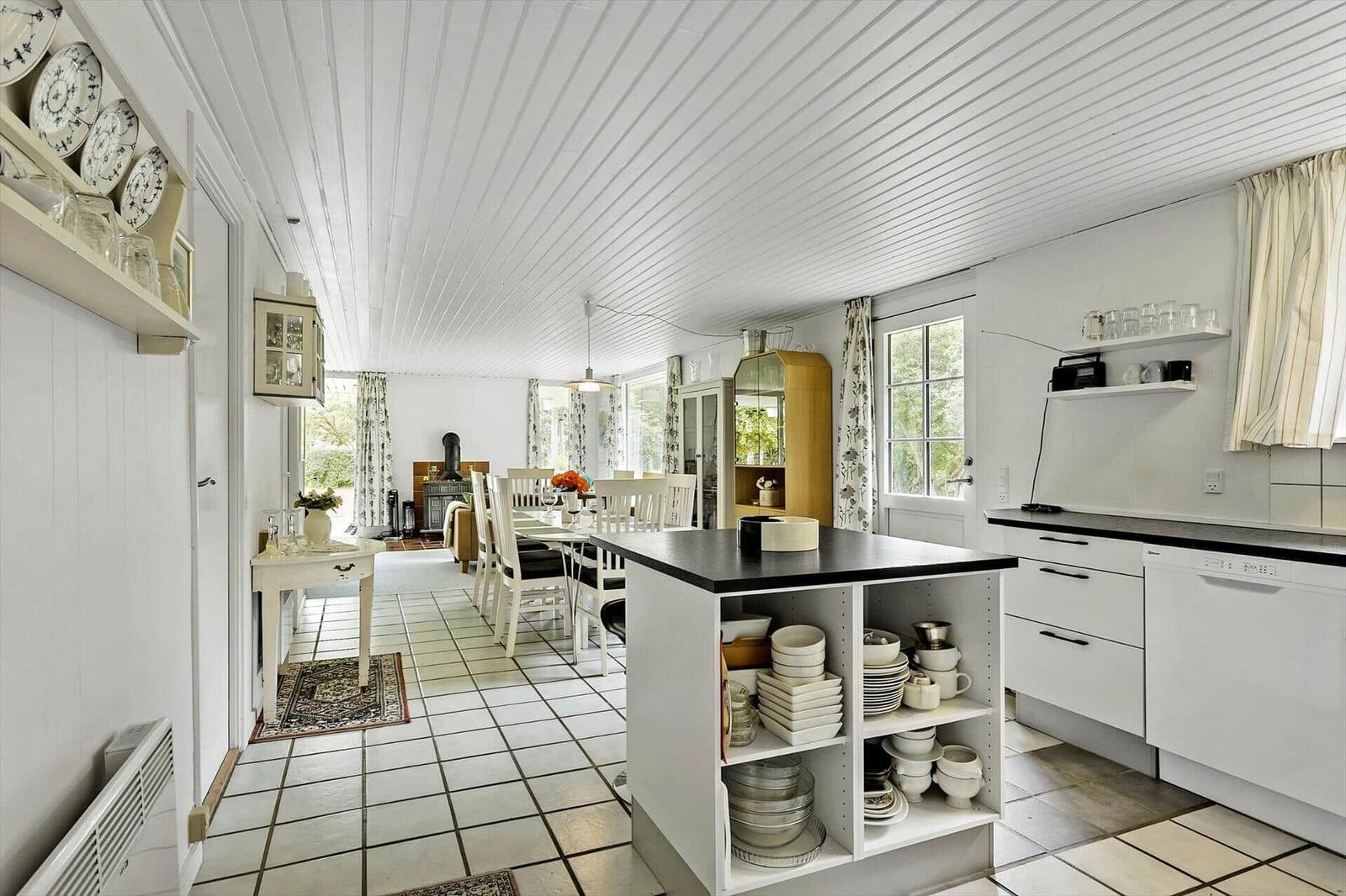 Kitchen with dining area, white cabinets, and black countertop. Windows and ceiling with wood paneling.
