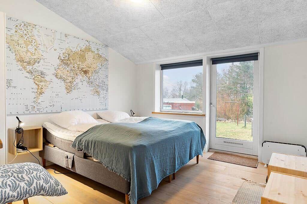 Bedroom with bed, world map on wall, and window to outdoor terrace.