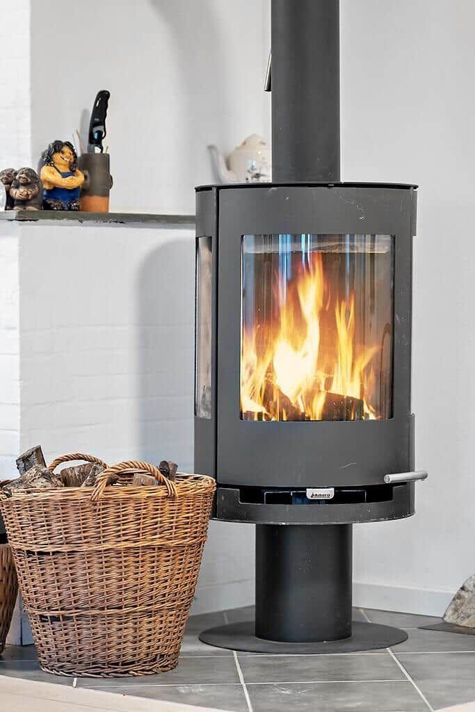 A wood-burning stove with burning logs, next to a basket of firewood and decorative figurines.