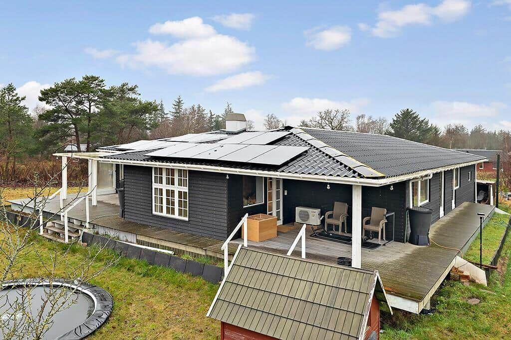 A dark house with solar panels, a terrace, and a trampoline in the garden.