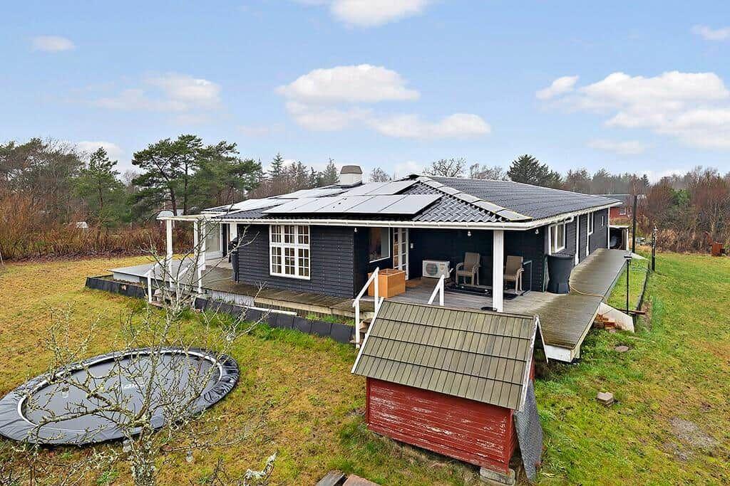 A dark blue vacation home with terrace, trampoline, and red shed in the grass.