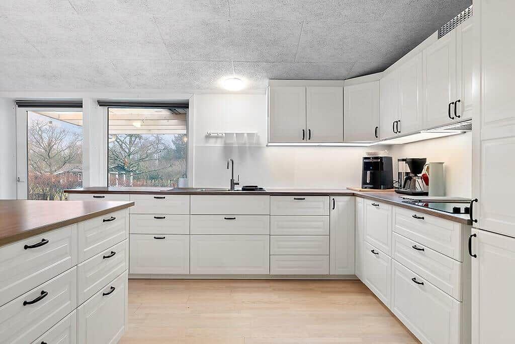 Kitchen with white cabinets, wooden countertops, and windows to the garden.
