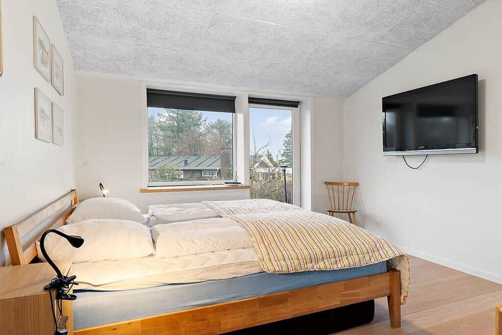 Bedroom with bed, windows, and TV mounted on the wall.