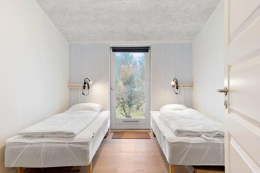 Two beds with white bedding face a glass door.