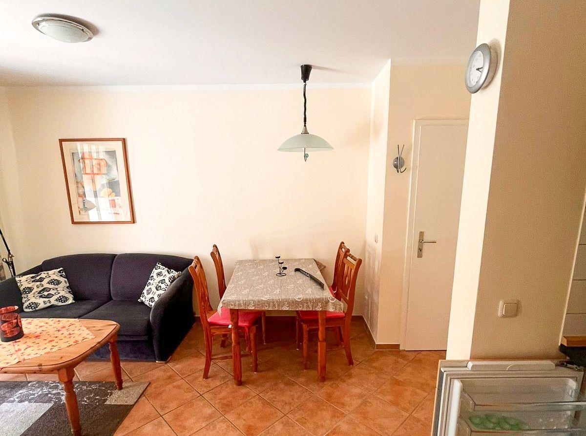Wohn- und Essbereich mit Sofa, Tisch und Stühlen. Wanduhr und Bild an der Wand.