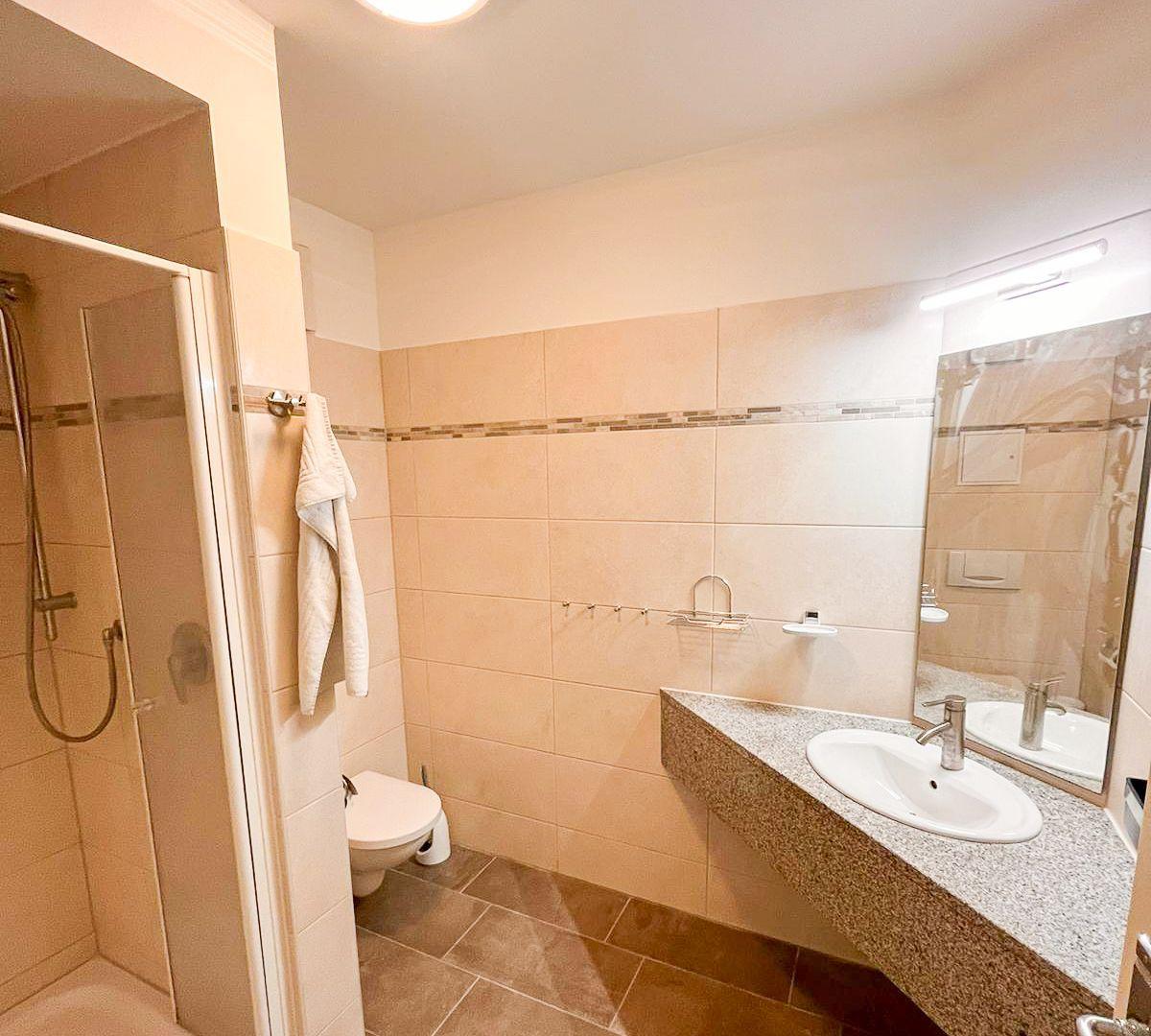 Badezimmer mit Dusche, Toilette und Waschbecken mit Spiegel.